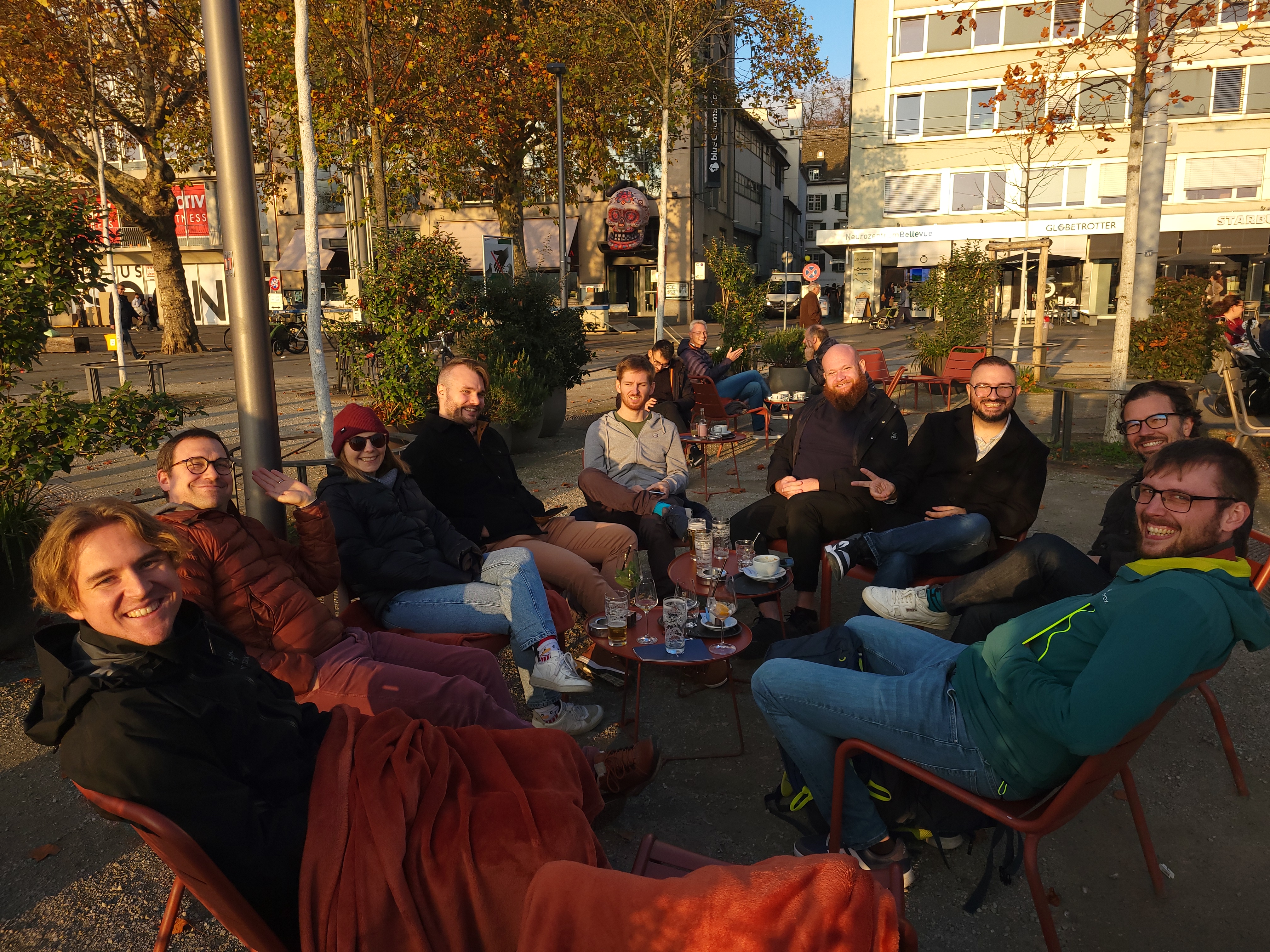 Nine Zitadel staff members smiling and posing at a bar near the Zurich opera house, with drinks on the table.