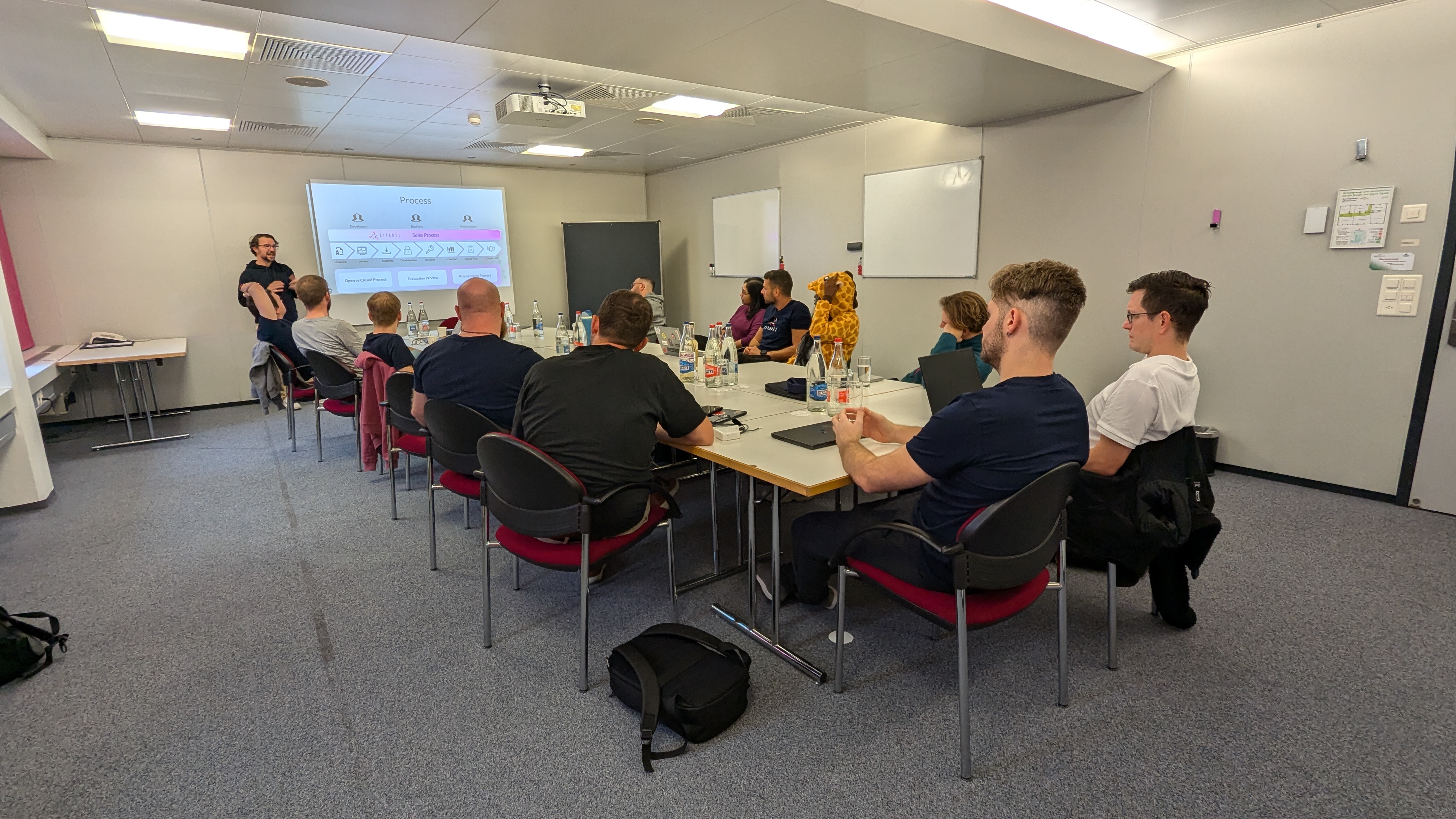 Zitadel staff in a meeting room, attentively watching Jason, the head of sales, present his workshop.