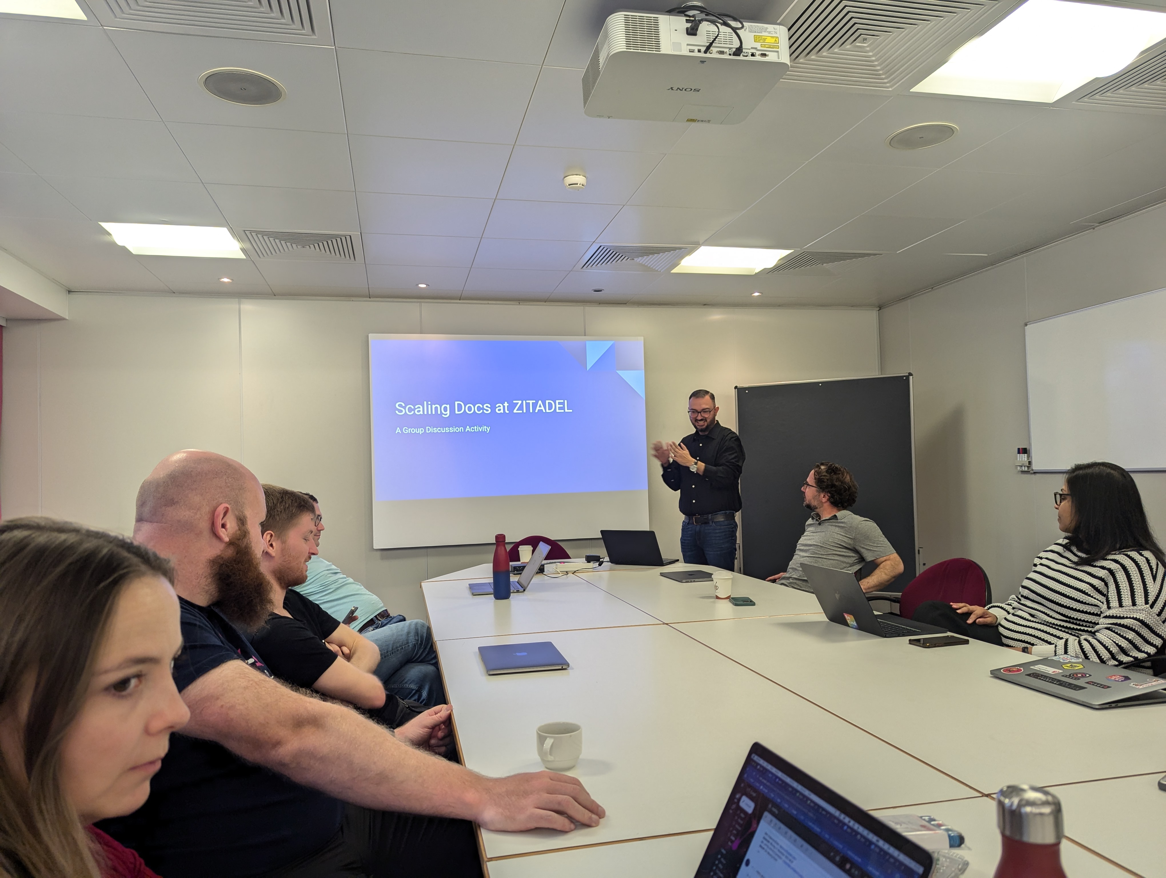 Zitadel staff in a meeting room, attentively watching Jim, the product marketing manager, present his workshop.