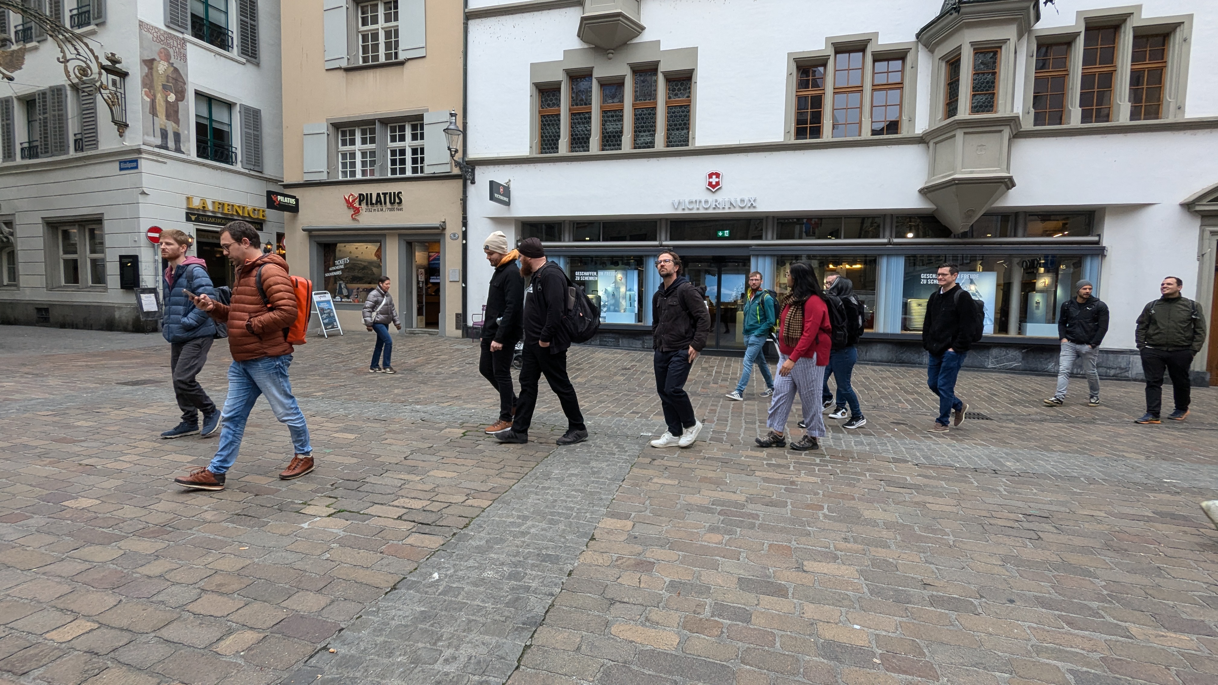 Team walking through Lucerne, passing buildings with signs for 'Pilatus', 'Victorinox', and 'La Fenice Steakhouse'.